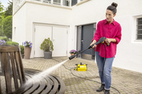 Person using a Kärcher high-pressure cleaner to wash a wooden bench in an outdoor patio setting.