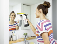 Woman using Kärcher window vac to clean bathroom mirror, with toiletries on the shelf below.