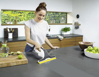 Person using a Kärcher window vac on a kitchen countertop, surrounded by apples, limes, and kitchen utensils.