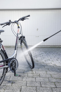 Bicycle being cleaned with a Kärcher high-pressure cleaner in front of a white garage door.