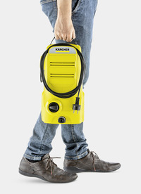 Person holding a yellow Kärcher high-pressure cleaner, wearing jeans and brown shoes, against a white background.