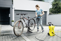 Person cleaning a muddy bicycle with a Kärcher high-pressure cleaner in a modern outdoor setting.