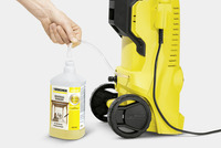 Hand connecting Kärcher universal cleaner bottle to a yellow Kärcher high-pressure cleaner via a clear tube.