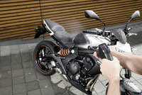 Hands using a Kärcher high-pressure cleaner to wash a black motorcycle outdoors on a tiled surface.