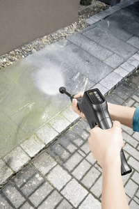 Hands using a Kärcher high-pressure cleaner to wash outdoor stone tiles, removing dirt and moss.