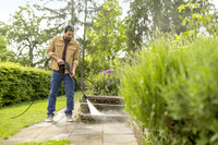 Man using Kärcher high-pressure cleaner on outdoor stone steps surrounded by lush greenery and trees.