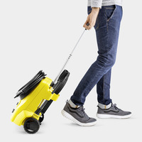 Person in jeans and trainers pulling a yellow Kärcher high-pressure cleaner on wheels with a handle.