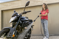 Person cleaning a black motorcycle with a Kärcher high-pressure cleaner in front of a modern garage.