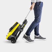 Person in jeans and trainers pulling a yellow Kärcher high-pressure cleaner on wheels.