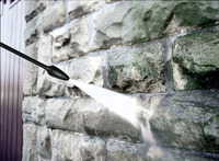 Kärcher high-pressure cleaner spraying water on a stone wall, removing dirt and grime.