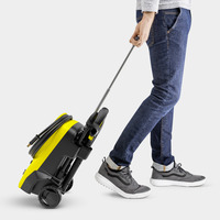 Person in jeans and trainers pulling a Kärcher high-pressure cleaner on wheels using a handle.