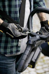 Person in checkered shirt and gloves holding a Kärcher high-pressure cleaner outdoors.