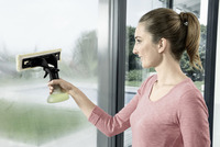 Woman using Kärcher window vac on large glass surface indoors.