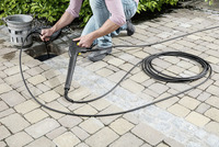 Person using a Kärcher high-pressure cleaner on outdoor paving stones, with coiled hose nearby.