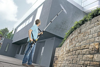 Man using Kärcher high-pressure cleaner on house exterior wall outdoors.
