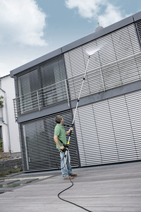 Man cleaning outdoor window blinds with a Kärcher high-pressure cleaner, standing on a wooden deck.