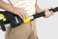 Person adjusting a Kärcher telescopic handle, wearing a striped shirt and beige trousers.