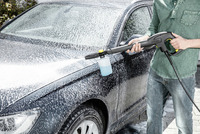 Person using Kärcher high-pressure cleaner to wash a car covered in soap suds outdoors.