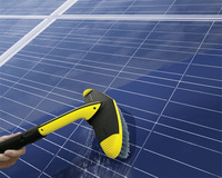 Hand cleaning solar panels with a Kärcher brush, showing reflection of sky on panel surface.