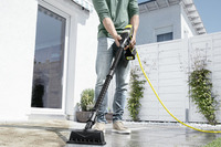 Person using a Kärcher high-pressure cleaner on a patio. Outdoor setting with white fence and plants in the background.