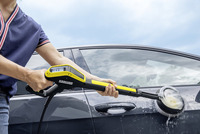 Person cleaning a car door with a Kärcher high-pressure cleaner, outdoors under a cloudy sky.