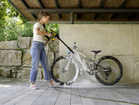 Person cleaning a muddy bicycle with a Kärcher high-pressure cleaner under a covered outdoor area with stone walls.