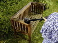 Person cleaning a wooden garden bench with a Kärcher brush attachment, surrounded by lush greenery.