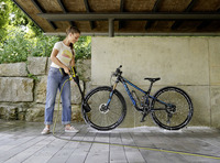 Person cleaning a mountain bike with a Kärcher high-pressure cleaner under a covered outdoor area, surrounded by stone walls and greenery.