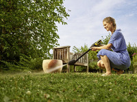 Person cleaning a large pot outdoors with a Kärcher high-pressure cleaner, surrounded by grass, trees, and a wooden bench.