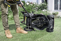 Person cleaning an overturned lawnmower with a Kärcher high-pressure cleaner in a garden setting.