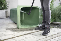 Person cleaning a green wheelie bin with a Kärcher high-pressure cleaner on a paved outdoor area.