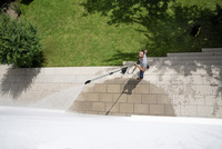 Person using a Kärcher high-pressure cleaner to wash outdoor stone steps, surrounded by grass and trees.