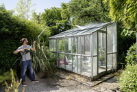 Person cleaning greenhouse roof with Kärcher high-pressure cleaner in a lush garden setting.