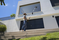 Man cleaning large window with Kärcher high-pressure cleaner outdoors on sunny day, standing on steps in front of modern white building.