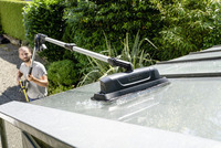 Kärcher high-pressure cleaner with extension wand cleaning a glass roof outdoors, surrounded by lush green foliage.
