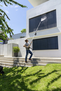 Man cleaning building facade with Kärcher high-pressure cleaner, standing on outdoor steps, surrounded by greenery.