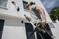 Man cleaning house exterior with Kärcher high-pressure cleaner, using an extension wand to reach upper windows.