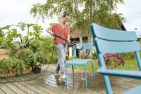 Person cleaning a blue outdoor chair with a Kärcher high-pressure cleaner on a wooden deck surrounded by plants and a garden setting.