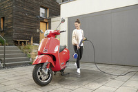 Person cleaning a red scooter with a Kärcher high-pressure cleaner in an outdoor setting with modern buildings.