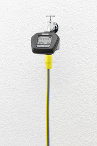 Kärcher water timer attached to a tap on a textured white wall, with a yellow hose connected below.