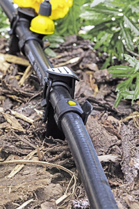 Kärcher garden irrigation system on soil, surrounded by mulch and green leaves.