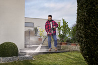 Person using Kärcher high-pressure cleaner on outdoor stone steps, surrounded by potted plants and garden.
