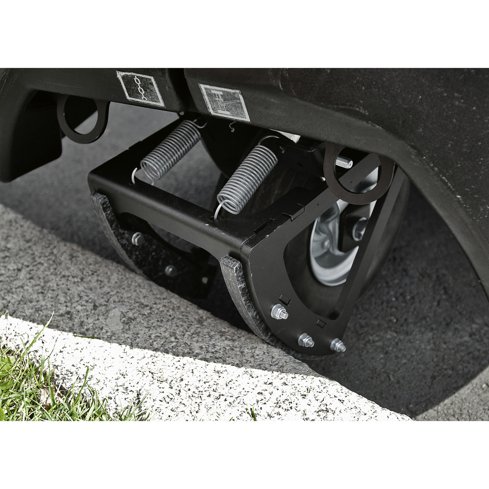 Close-up of a vehicle's suspension system with springs and bolts, positioned on a concrete kerb near grass. Close-up of a vehicle's suspension system with springs and bolts, positioned on a concrete kerb near grass.