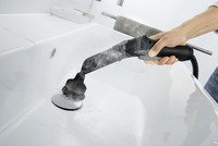 Hand using Kärcher steam cleaner on white sink surface indoors.