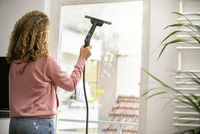 Woman cleaning a window with a Kärcher steam cleaner indoors, visible handprints on the glass.