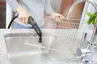 Person cleaning oven rack with Kärcher steam cleaner over kitchen sink.