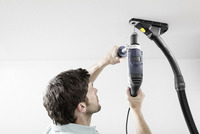 Person using a drill on a ceiling with a Kärcher dust extractor attached, indoors.