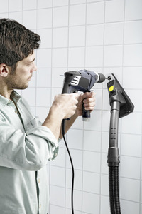 Man using a drill on tiled wall with Kärcher dust extractor attached.