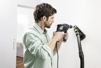 Man using a drill on a white wall indoors, with a Kärcher vacuum cleaner attached to collect dust.