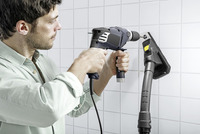 Man using a drill on a tiled wall next to a Kärcher steam cleaner.